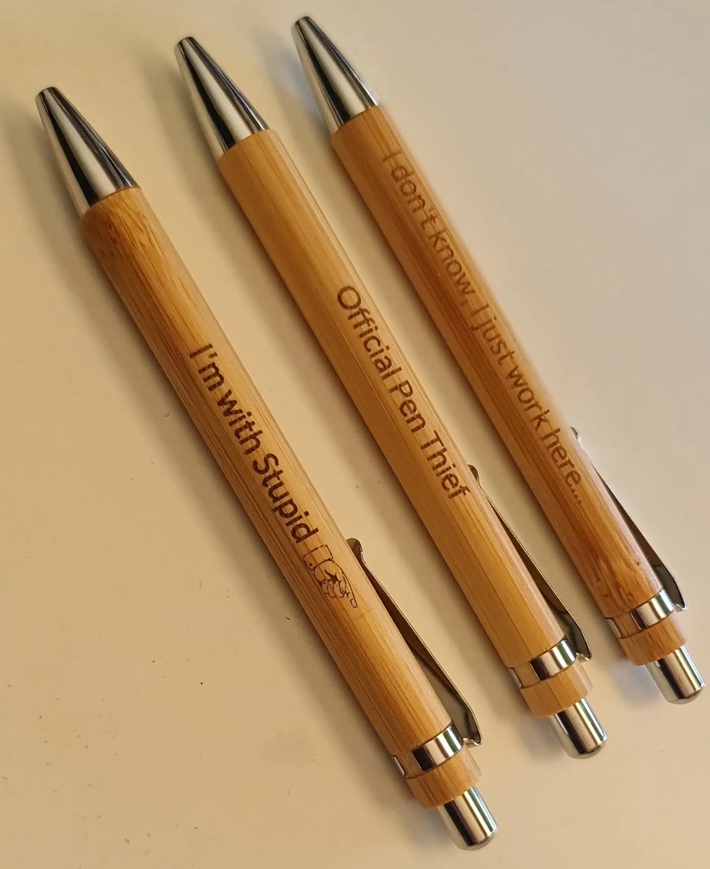 Three wooden pens with engraved text on a beige background